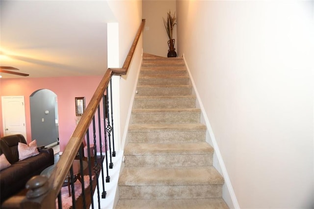 stairway with arched walkways, carpet, baseboards, and a ceiling fan