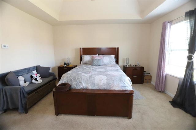 bedroom with baseboards, a raised ceiling, and light colored carpet