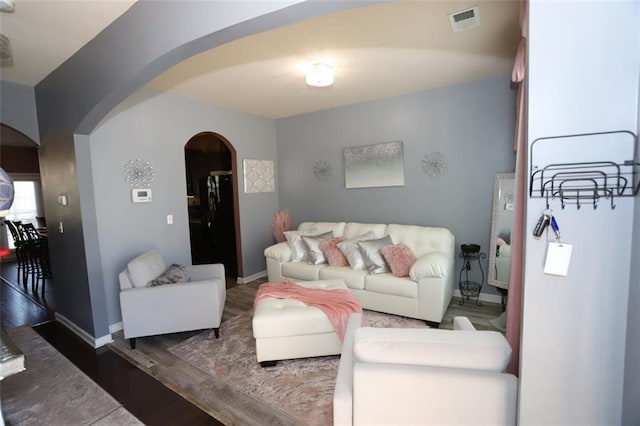 living area with visible vents, baseboards, arched walkways, and wood finished floors