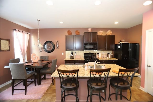 kitchen with a kitchen bar, tasteful backsplash, a kitchen island with sink, and black appliances