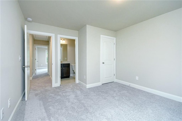 unfurnished bedroom featuring baseboards, attic access, light carpet, and ensuite bath
