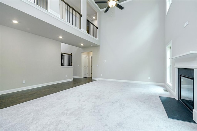 unfurnished living room with a fireplace with flush hearth, ceiling fan, carpet floors, baseboards, and a high ceiling