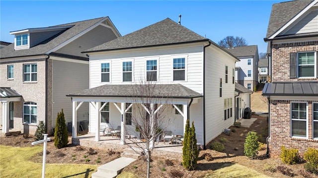 rear view of property featuring a patio, a standing seam roof, a shingled roof, brick siding, and metal roof