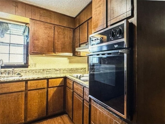 kitchen with a textured ceiling, light wood-type flooring, black appliances, sink, and light stone counters