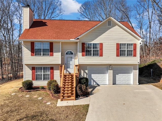 raised ranch featuring driveway, an attached garage, a chimney, and a shingled roof