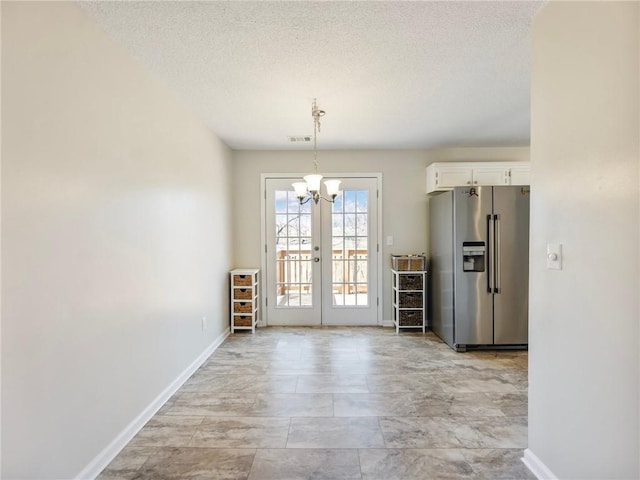 unfurnished dining area featuring visible vents, a textured ceiling, french doors, an inviting chandelier, and baseboards