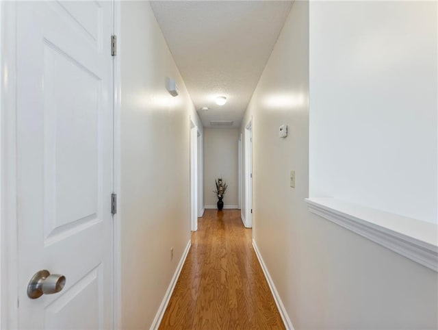 hall with baseboards, light wood-style floors, and a textured ceiling