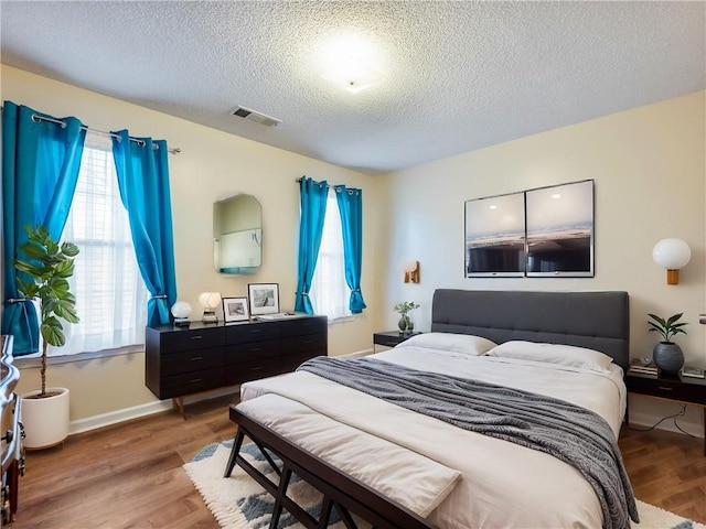 bedroom featuring visible vents, a textured ceiling, baseboards, and wood finished floors