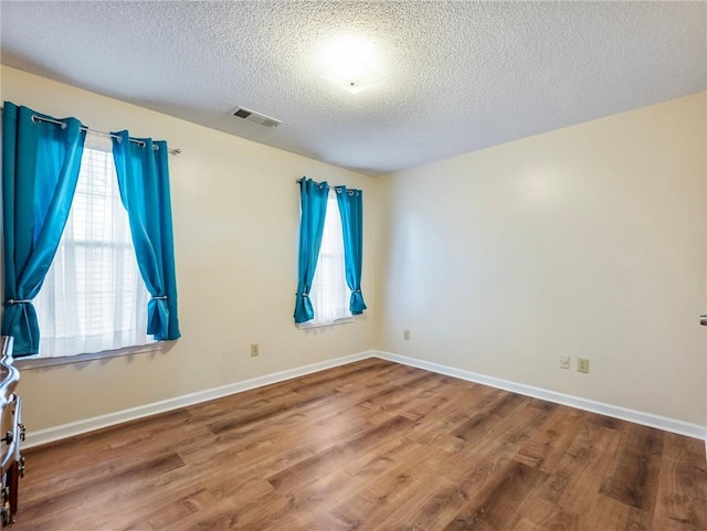 unfurnished room featuring visible vents, a textured ceiling, baseboards, and wood finished floors