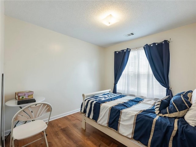 bedroom with visible vents, baseboards, a textured ceiling, and wood finished floors