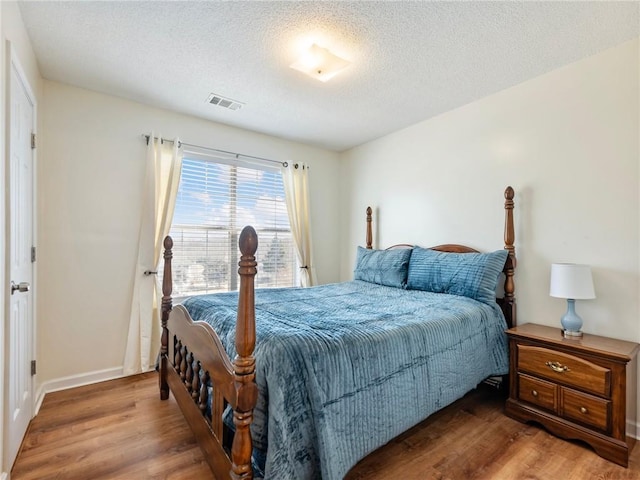 bedroom featuring wood finished floors, visible vents, and a textured ceiling