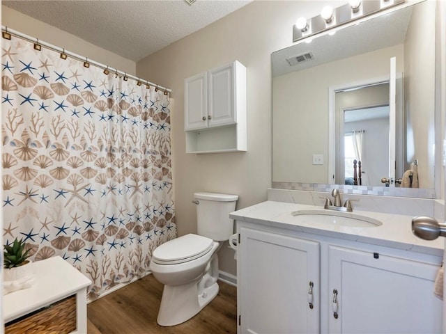 bathroom featuring visible vents, toilet, a textured ceiling, wood finished floors, and vanity