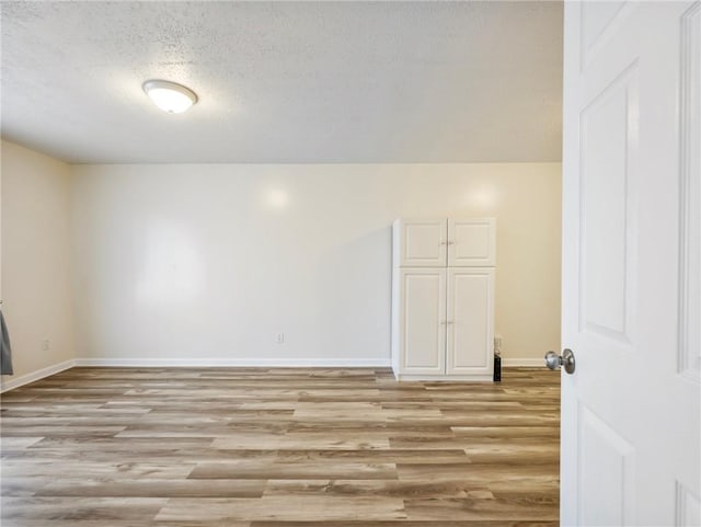 unfurnished room with baseboards, light wood finished floors, and a textured ceiling