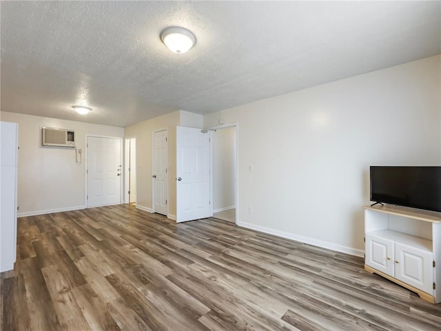 unfurnished living room featuring a wall mounted air conditioner, baseboards, a textured ceiling, and wood finished floors