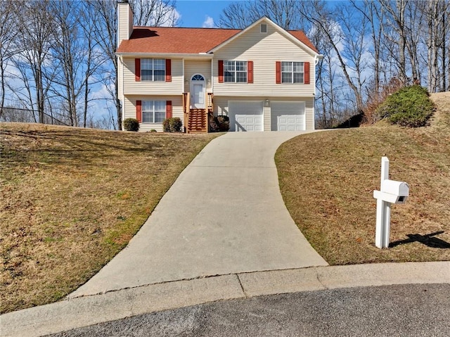 raised ranch featuring a garage, driveway, a front yard, and a chimney