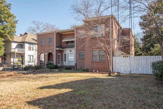 view of property featuring brick siding, a front lawn, and fence