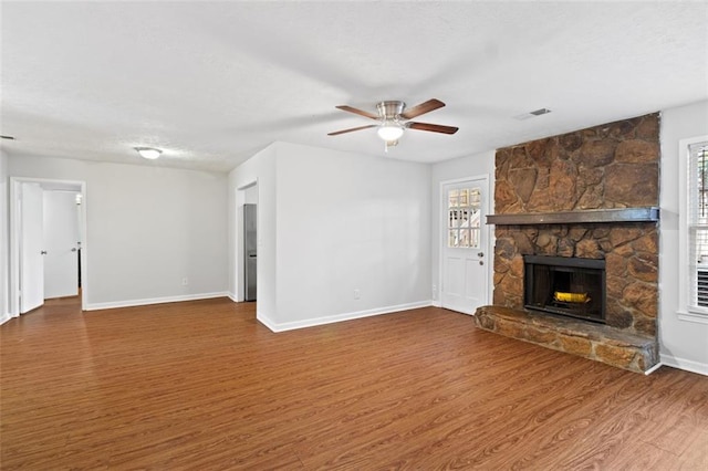 unfurnished living room with baseboards, ceiling fan, visible vents, a fireplace, and wood finished floors