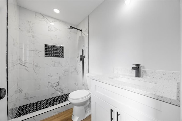 bathroom featuring a tile shower, hardwood / wood-style floors, vanity, and toilet