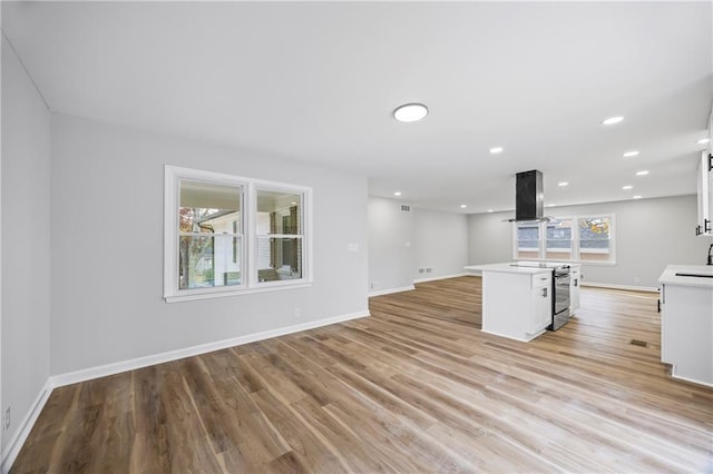 kitchen featuring white cabinets, island range hood, stainless steel electric range oven, and light hardwood / wood-style floors