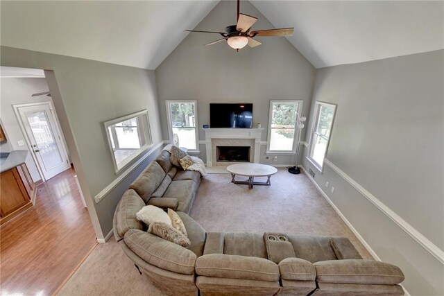 living room featuring ceiling fan, light wood-type flooring, high vaulted ceiling, and a fireplace