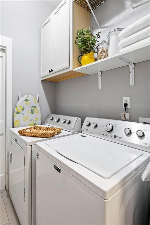 washroom featuring light tile patterned floors, cabinet space, and washing machine and clothes dryer