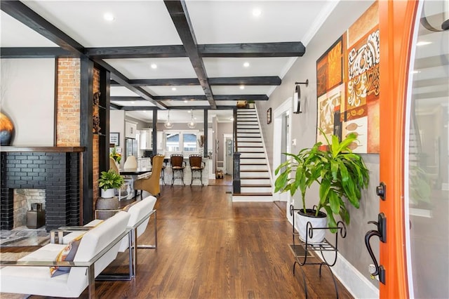 foyer entrance with beam ceiling, coffered ceiling, wood finished floors, a brick fireplace, and stairs