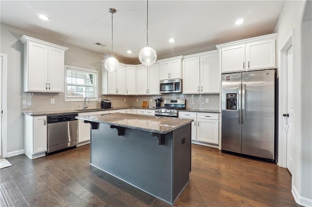 kitchen featuring white cabinetry, stainless steel appliances, dark hardwood / wood-style floors, decorative light fixtures, and a kitchen island