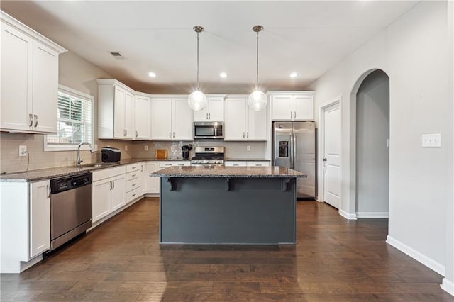 kitchen with white cabinets, appliances with stainless steel finishes, a kitchen island, and dark wood-type flooring