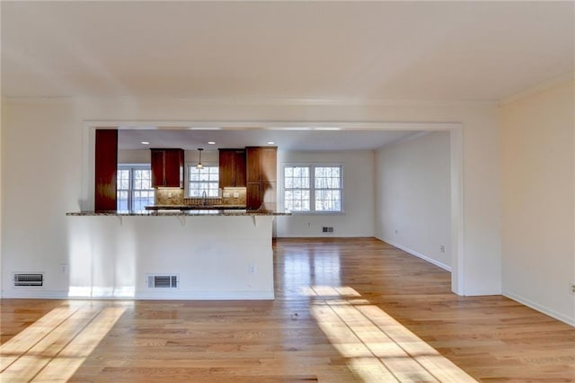 unfurnished living room featuring sink, crown molding, and light wood-type flooring