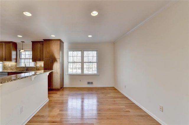 kitchen with sink, light stone counters, hanging light fixtures, light hardwood / wood-style floors, and decorative backsplash