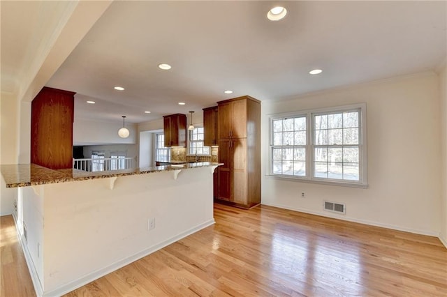 kitchen with a kitchen bar, light stone counters, light wood-type flooring, kitchen peninsula, and pendant lighting