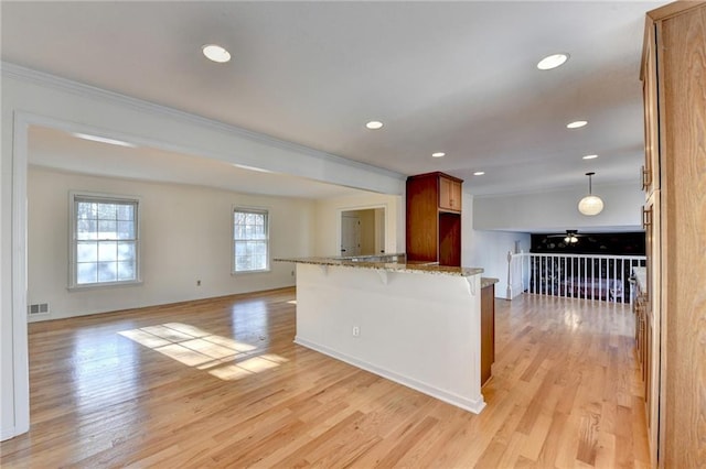 kitchen featuring decorative light fixtures, a breakfast bar area, kitchen peninsula, light stone countertops, and light hardwood / wood-style flooring