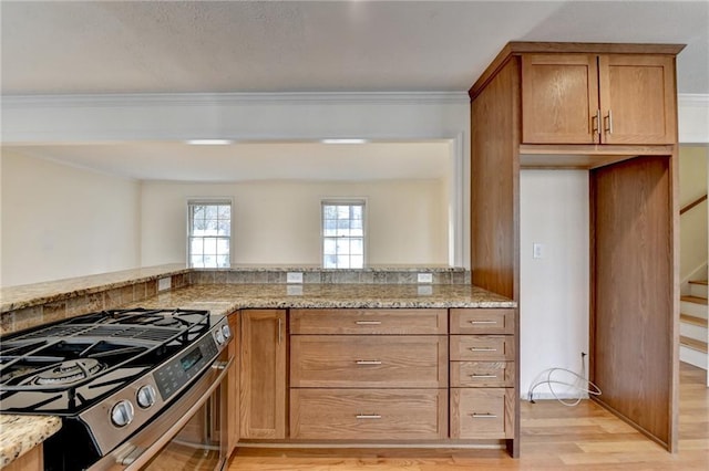 kitchen with ornamental molding, stainless steel range with gas cooktop, light wood-type flooring, and light stone counters