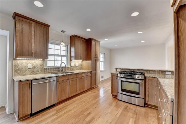 kitchen with appliances with stainless steel finishes, decorative light fixtures, sink, light stone countertops, and light hardwood / wood-style flooring