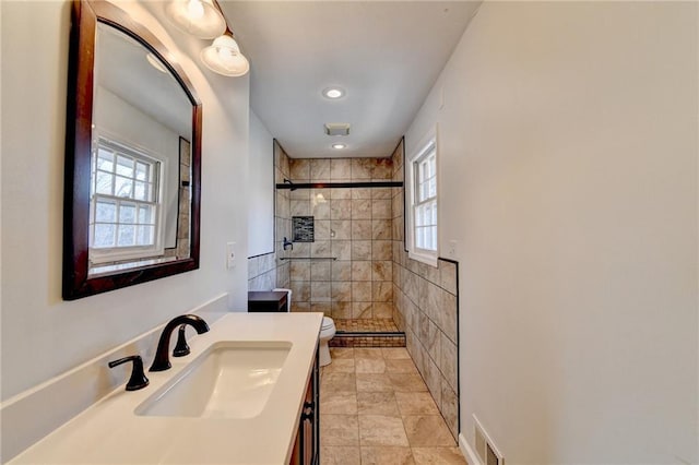 bathroom with vanity, a wealth of natural light, toilet, and tiled shower