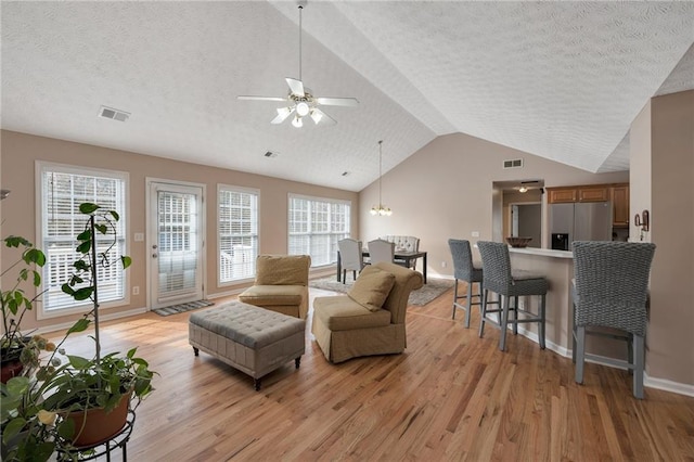 living room featuring lofted ceiling, a textured ceiling, a wealth of natural light, and light hardwood / wood-style flooring