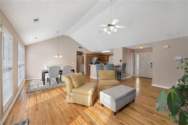 living room with ceiling fan with notable chandelier, lofted ceiling, and light hardwood / wood-style flooring