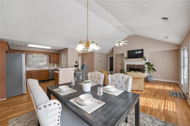 dining room with light hardwood / wood-style flooring, ceiling fan with notable chandelier, vaulted ceiling, and sink