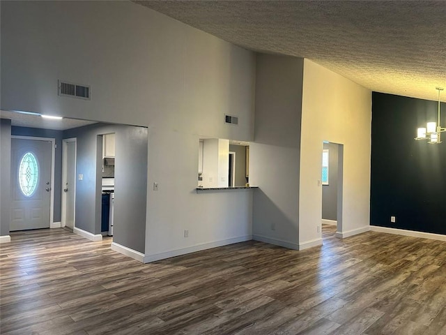 unfurnished living room with a textured ceiling, dark hardwood / wood-style flooring, a notable chandelier, and a high ceiling