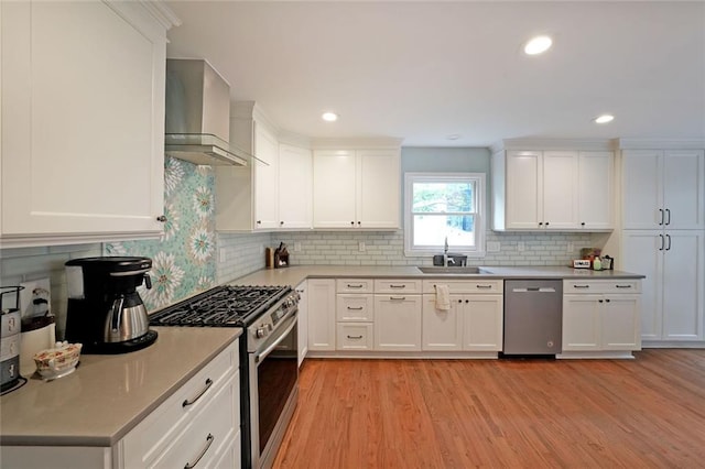 kitchen featuring light wood-style floors, wall chimney range hood, tasteful backsplash, a sink, and stainless steel appliances