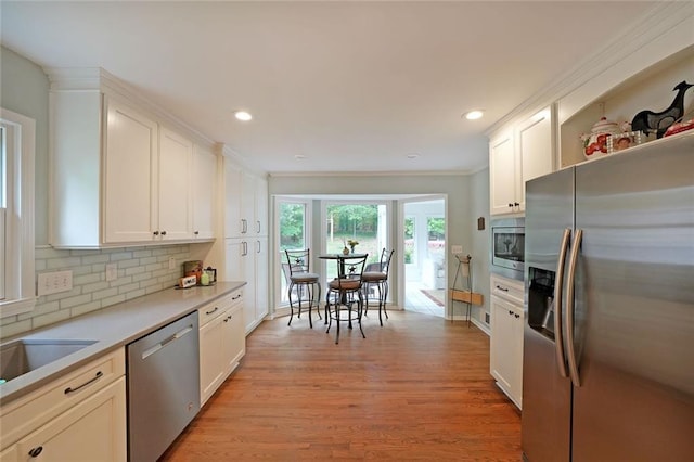 kitchen with backsplash, white cabinets, appliances with stainless steel finishes, and light wood-type flooring