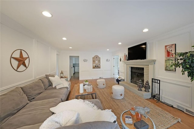 living room featuring a brick fireplace, wood finished floors, ornamental molding, a decorative wall, and recessed lighting