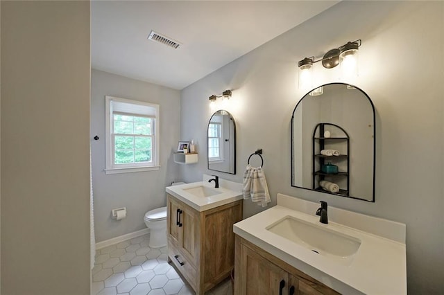 bathroom with toilet, visible vents, two vanities, and a sink