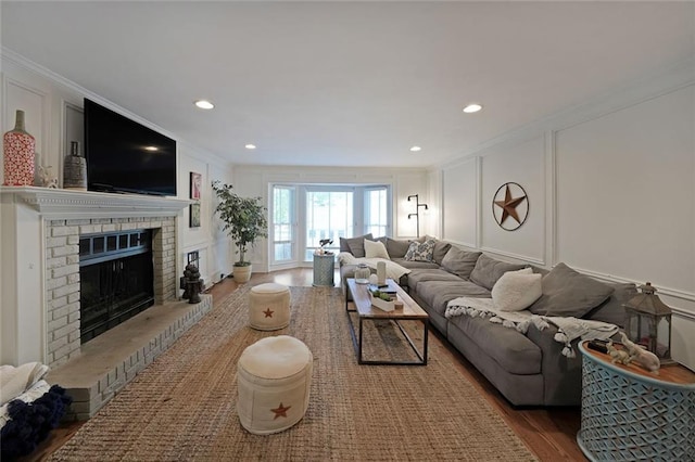 living area featuring crown molding, a fireplace, a decorative wall, and wood finished floors