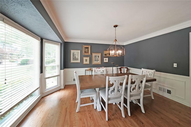 dining space with crown molding, visible vents, light wood-style floors, a wainscoted wall, and a chandelier
