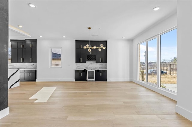 unfurnished living room with recessed lighting, beverage cooler, light wood-style flooring, and wet bar