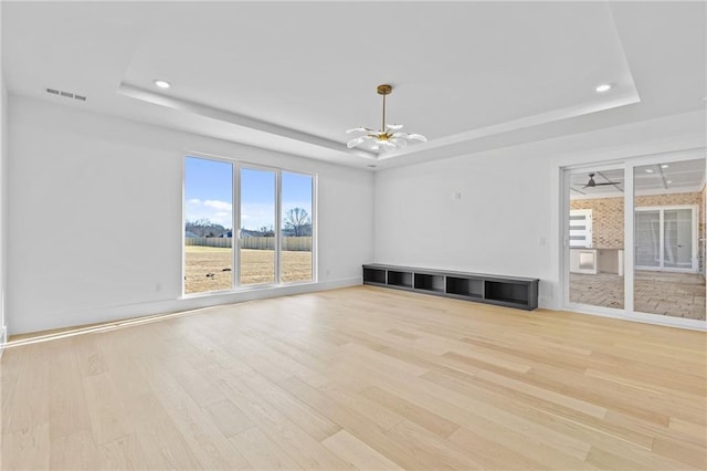 unfurnished living room featuring light wood-type flooring, a raised ceiling, and visible vents