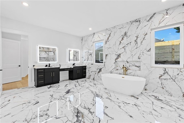 full bathroom with marble finish floor, double vanity, recessed lighting, a soaking tub, and stone wall