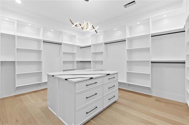 spacious closet featuring light wood-style floors and an inviting chandelier