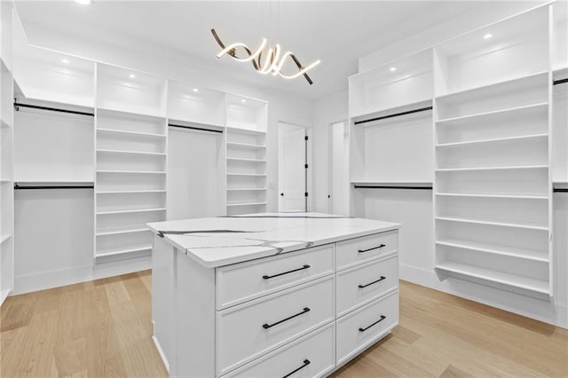 spacious closet featuring light wood-style floors, an inviting chandelier, and a barn door